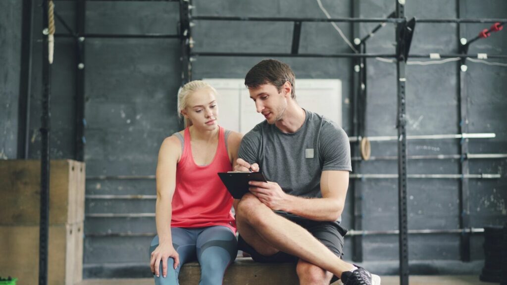 Two gym members logging their workout intensity in a notebook to ensure consistent progressive overload.