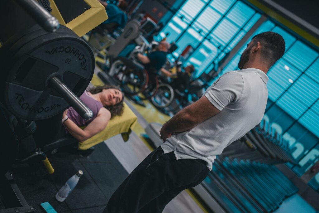 A supportive gym partner assisting a beginner with proper lifting form during a strength workout.