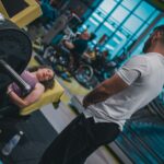 A supportive gym partner assisting a beginner with proper lifting form during a strength workout.