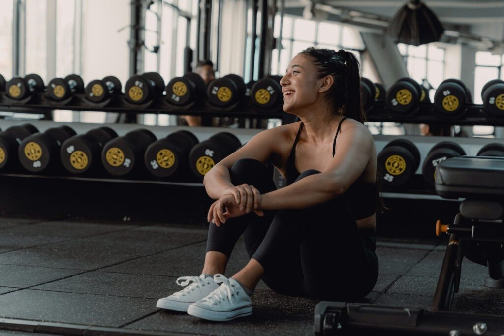 Woman resting and laughing during a gym session to recover from a fitness plateau.