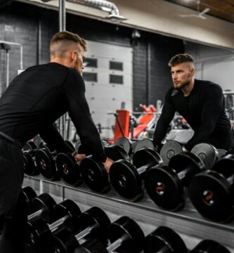 man in black long sleeve shirt and black pants carrying black dumbbell