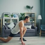 A person in athletic wear performing a focused bodyweight squat in a bright, modern, minimalist living room with natural light.