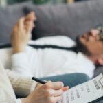 a person laying on a couch writing on a piece of paper
